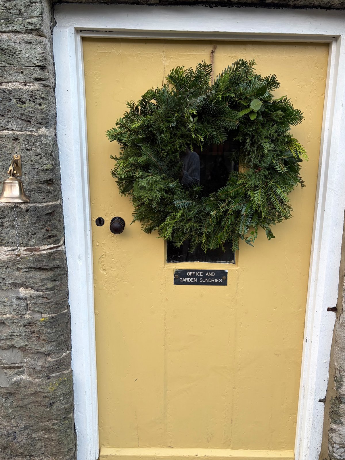 A full evergreen Christmas wreath hanging on the yellow garden shop door