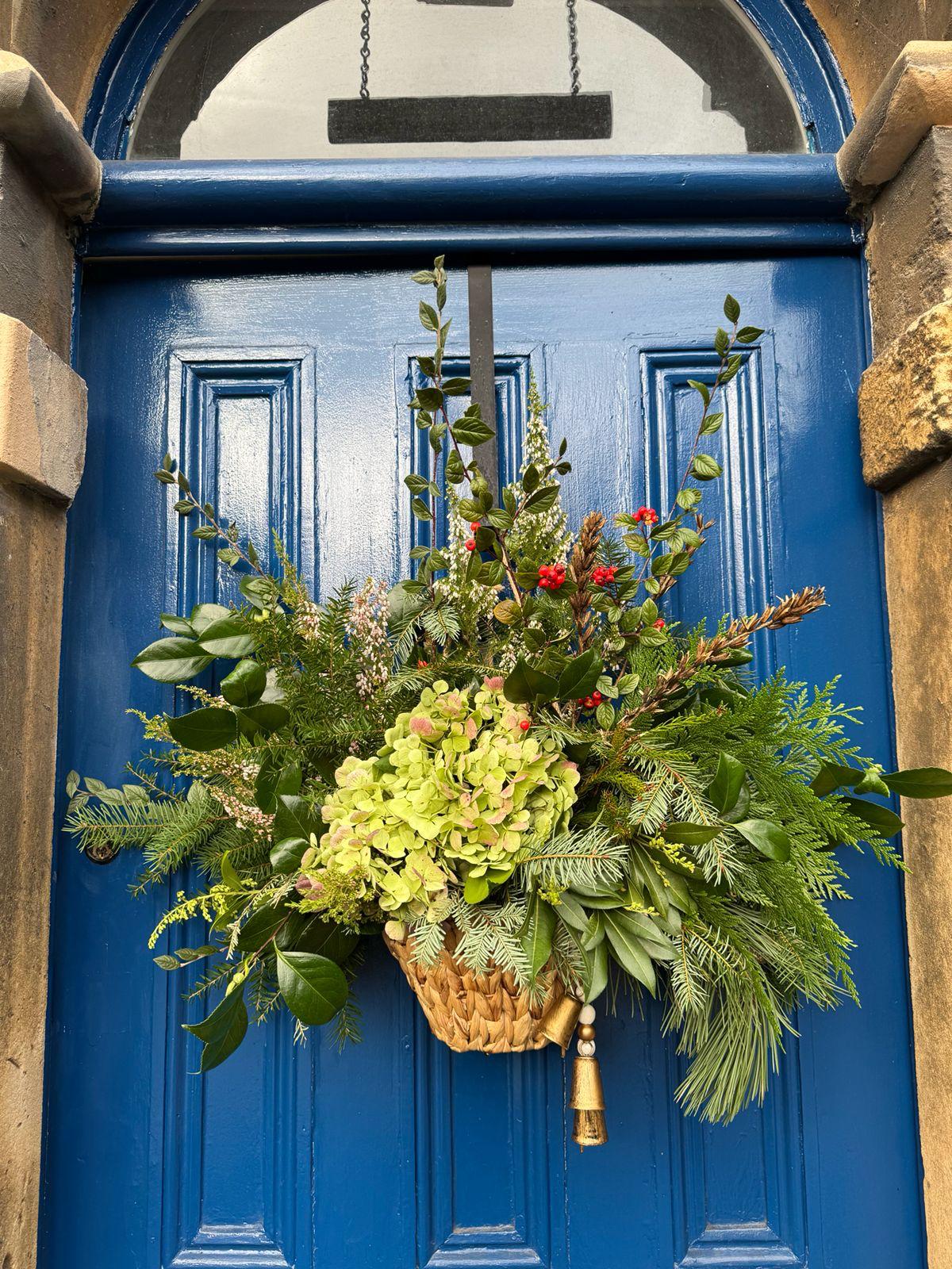 A woven door basket filled with hydrangea, evergreen foliage and berries on a blue door