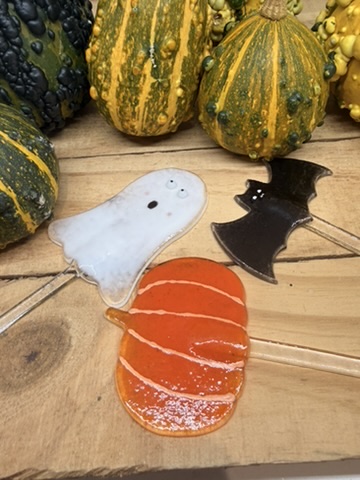 Fused glass ghost, bat and orange pumpkin decorations beside autumn gourds