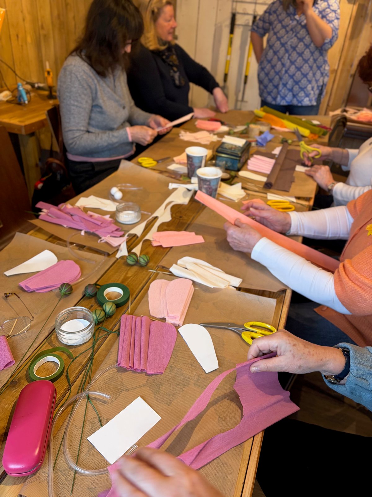 Workshop guests making flowers from pink and cream crepe paper around the table