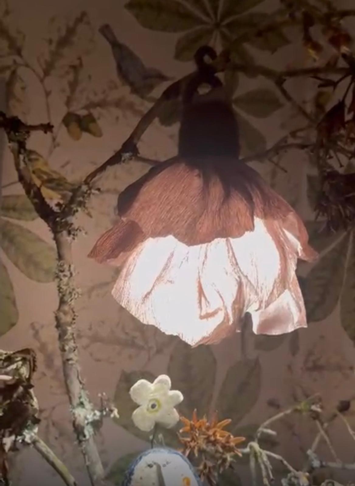 A glowing flower shaped crepe paper lampshade hanging among twigs