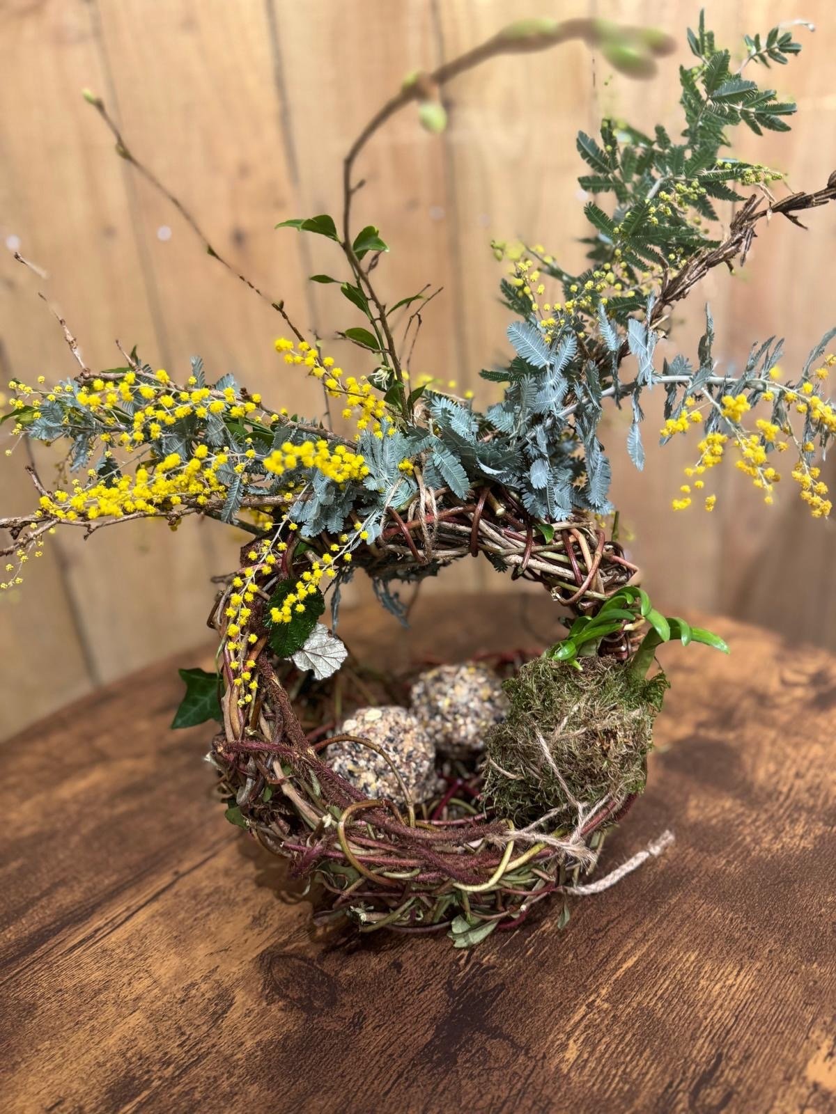 A woven twig nest decorated with moss, foliage and yellow flowers